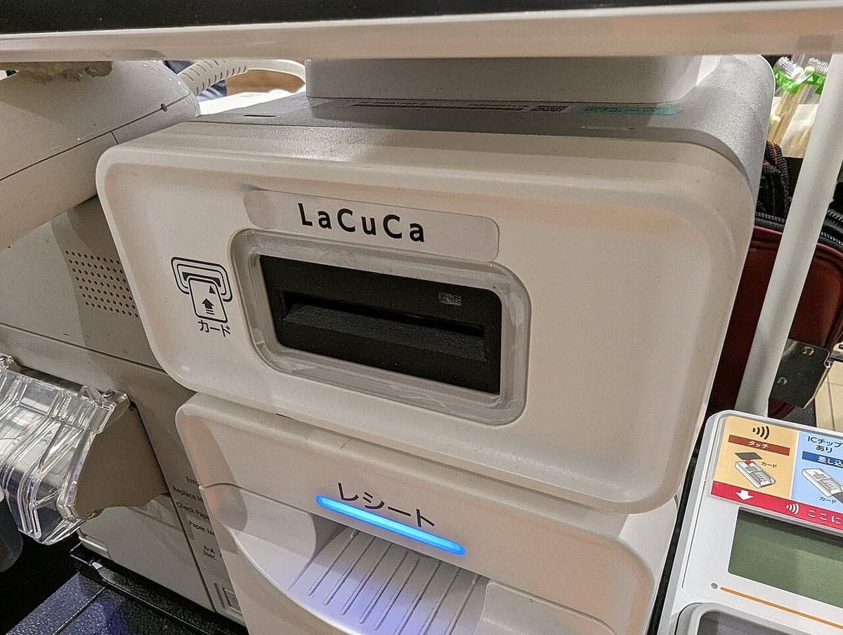 Meja kasir supermarket dengan terminal pembayaran, printer struk, dan laci uang